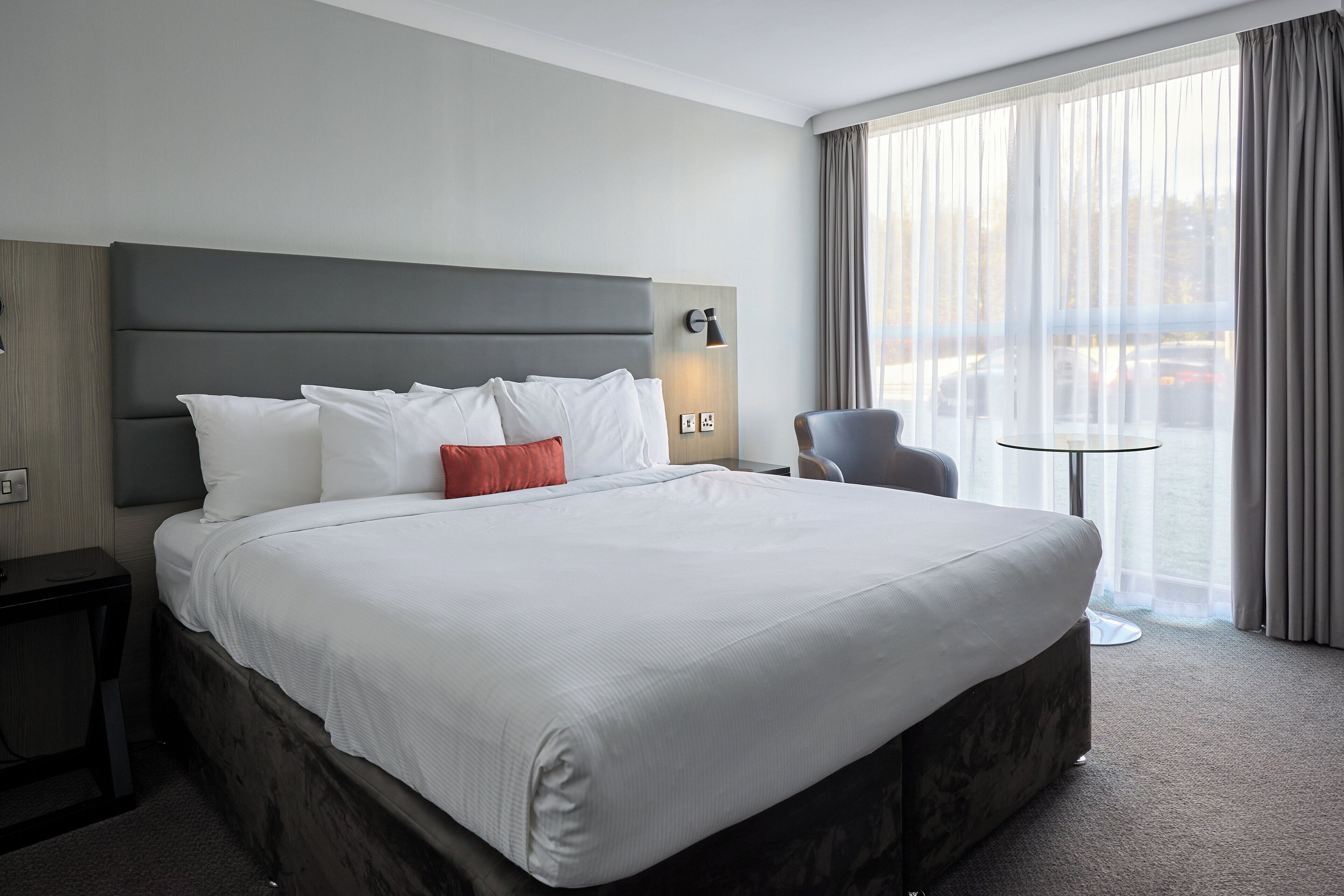 Hotellihuone, jossa on suuri sänky, yöpöytä, tuoli ja pieni pöytä.