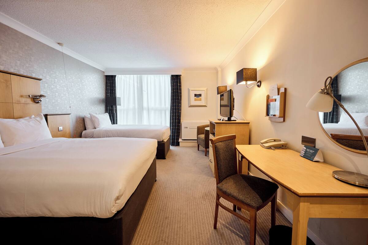 A hotel room with two beds, a desk, a chair, a desk lamp, a telephone, and a mirror.