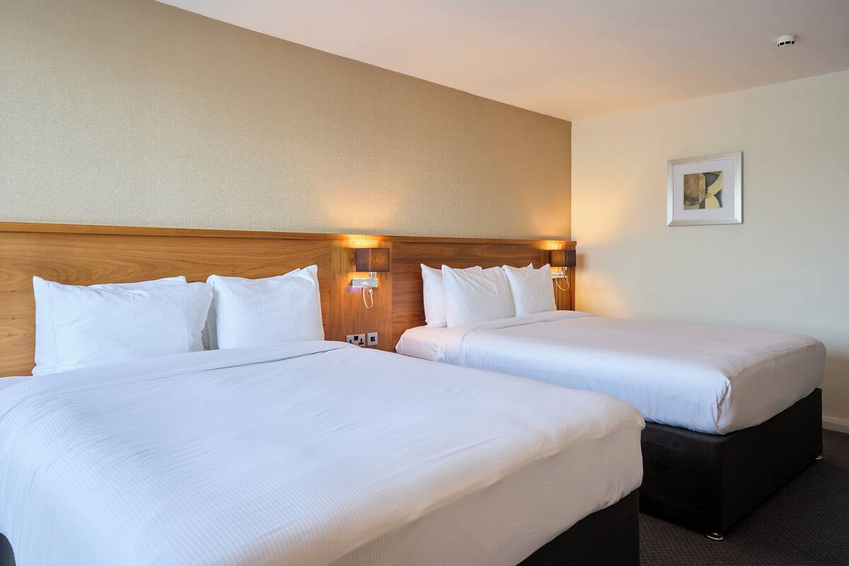 A hotel room with two beds, wooden headboards, and wall-mounted lamps.