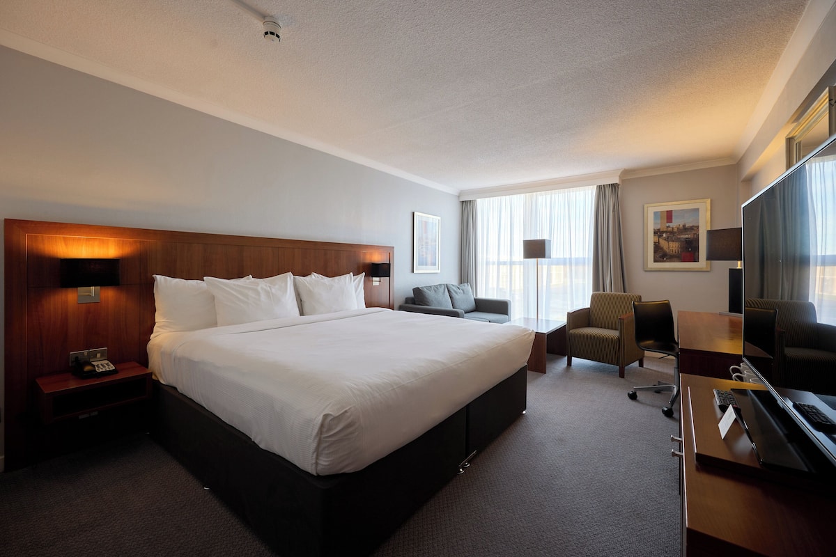 A hotel room with a large bed, a desk with a computer, a chair, and a TV.