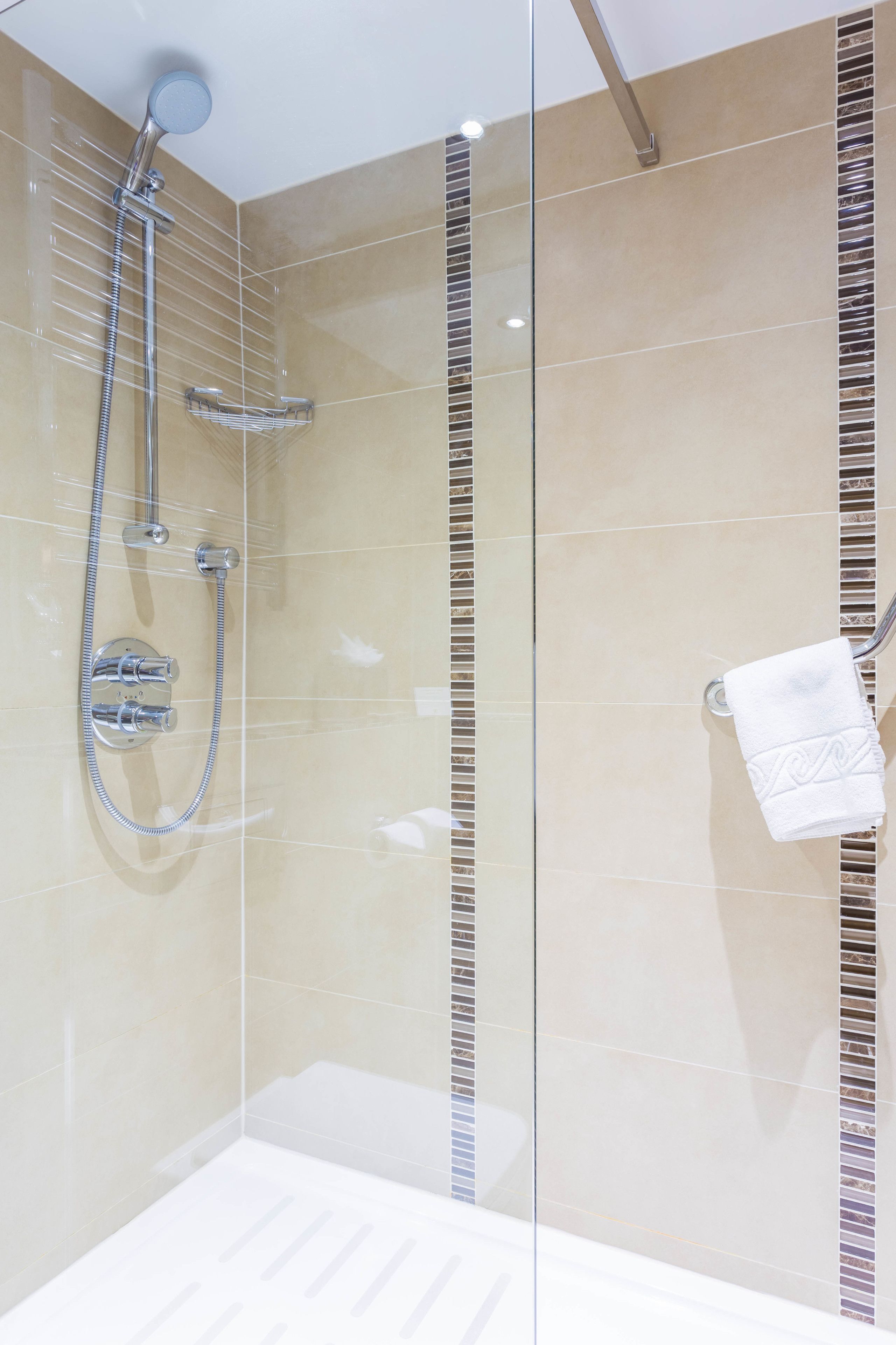 A modern bathroom with a glass shower enclosure, a chrome showerhead, and a towel rack with a folded towel.