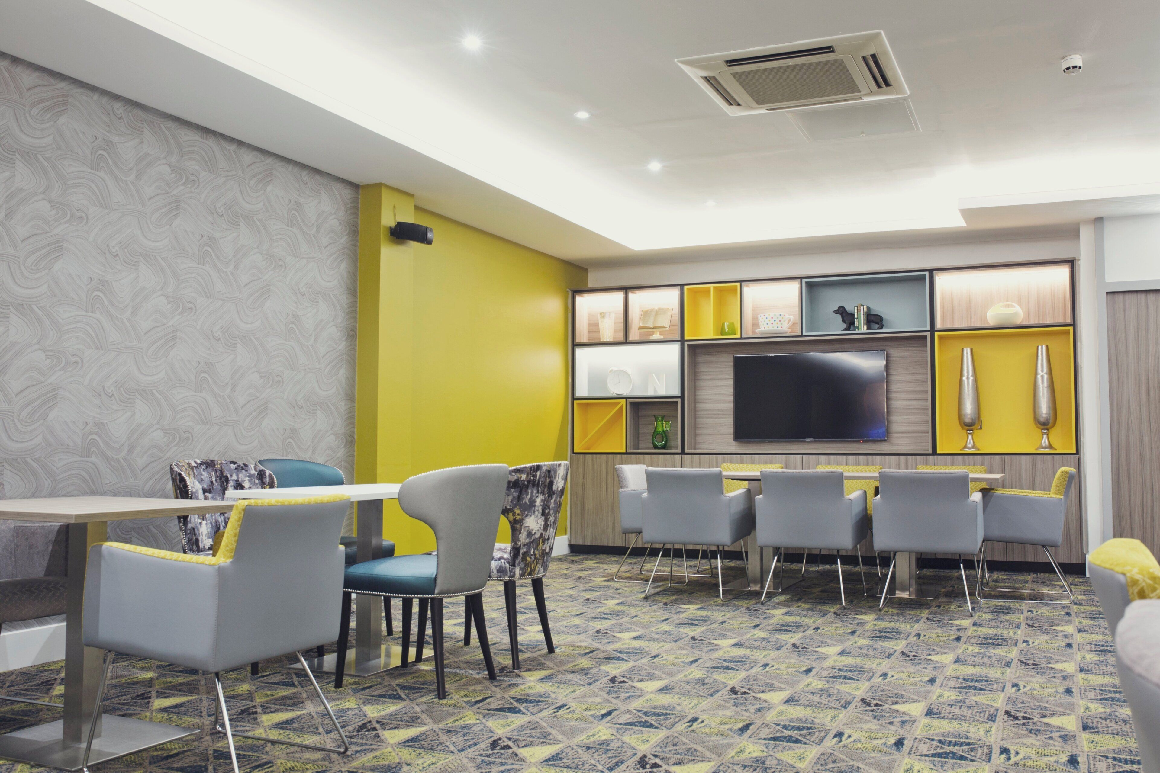 Une chambre d’hôtel moderne dotée d’un coin repas, d’un téléviseur à écran plat et d’une moquette à motifs.