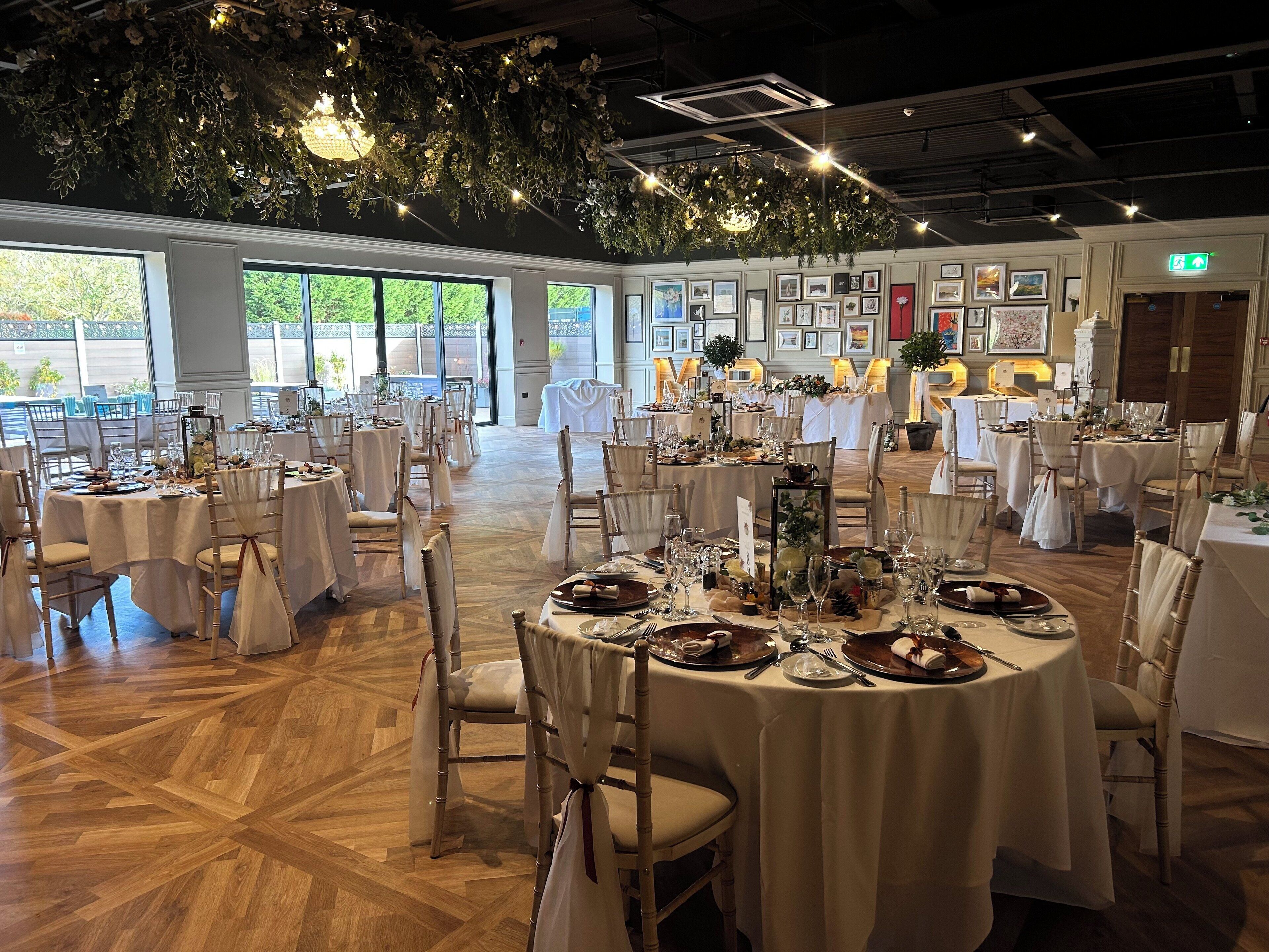Une salle de banquet avec des tables rondes dressées pour le repas, de grandes fenêtres et des œuvres d’art encadrées accrochées aux murs.