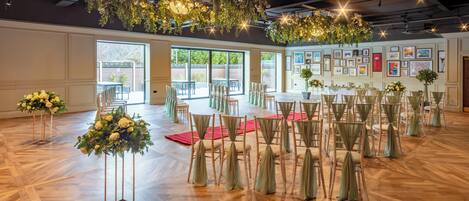 Un vaste hall doté d’un plancher en bois, de rangées de chaises ornées de rubans verts et de décorations florales.