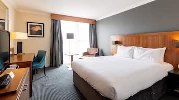 Een hotelkamer met een groot bed, een bureau met lamp, een stoel en een kleine tafel.
