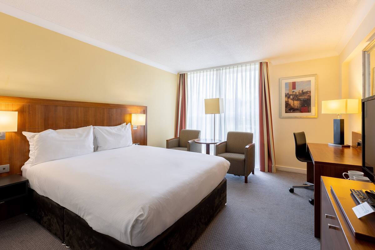 A hotel room with a large bed, a desk with a computer, a chair, and a small table.