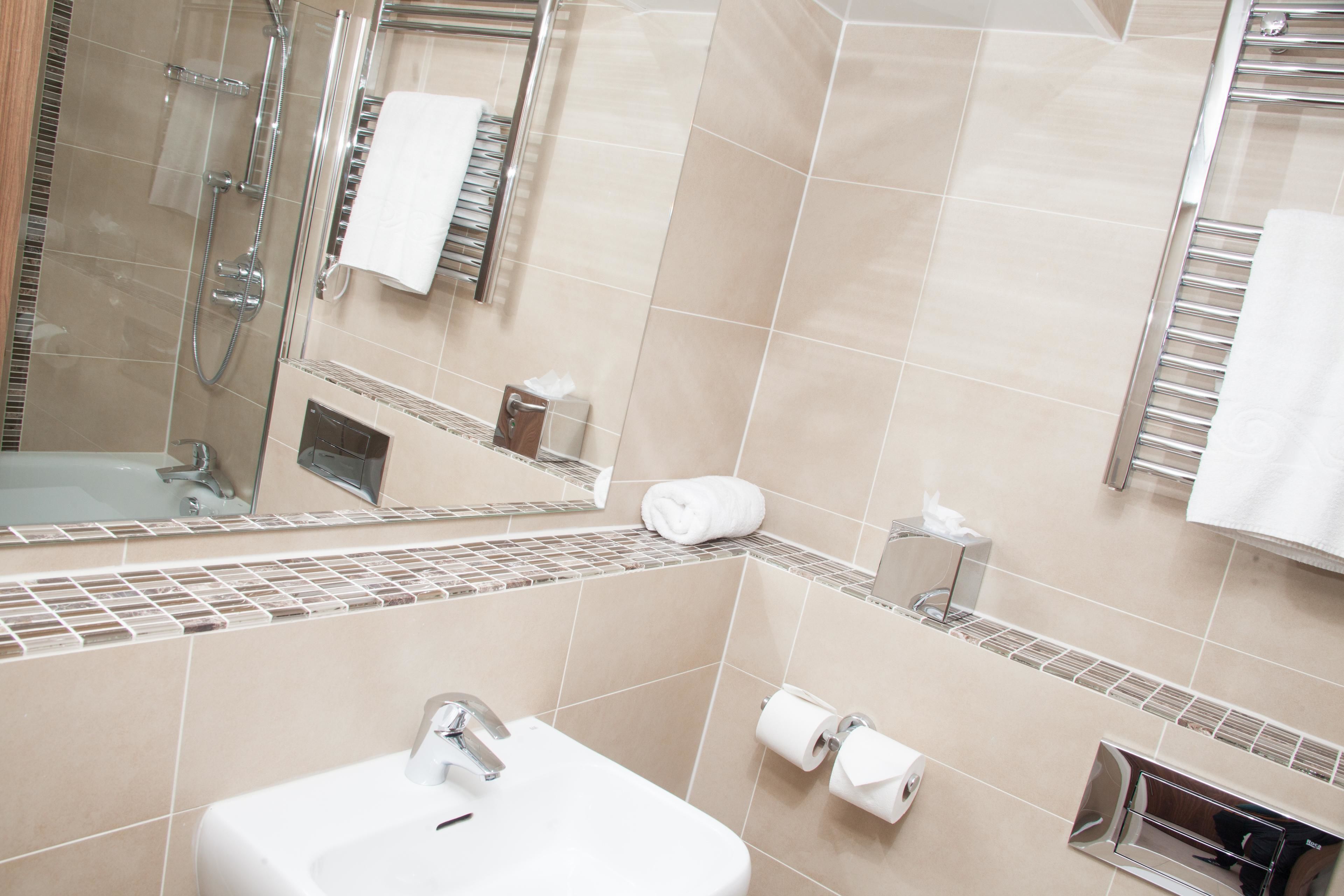 Een moderne badkamer met een wastafel, spiegel, handdoekhouder en douche.
