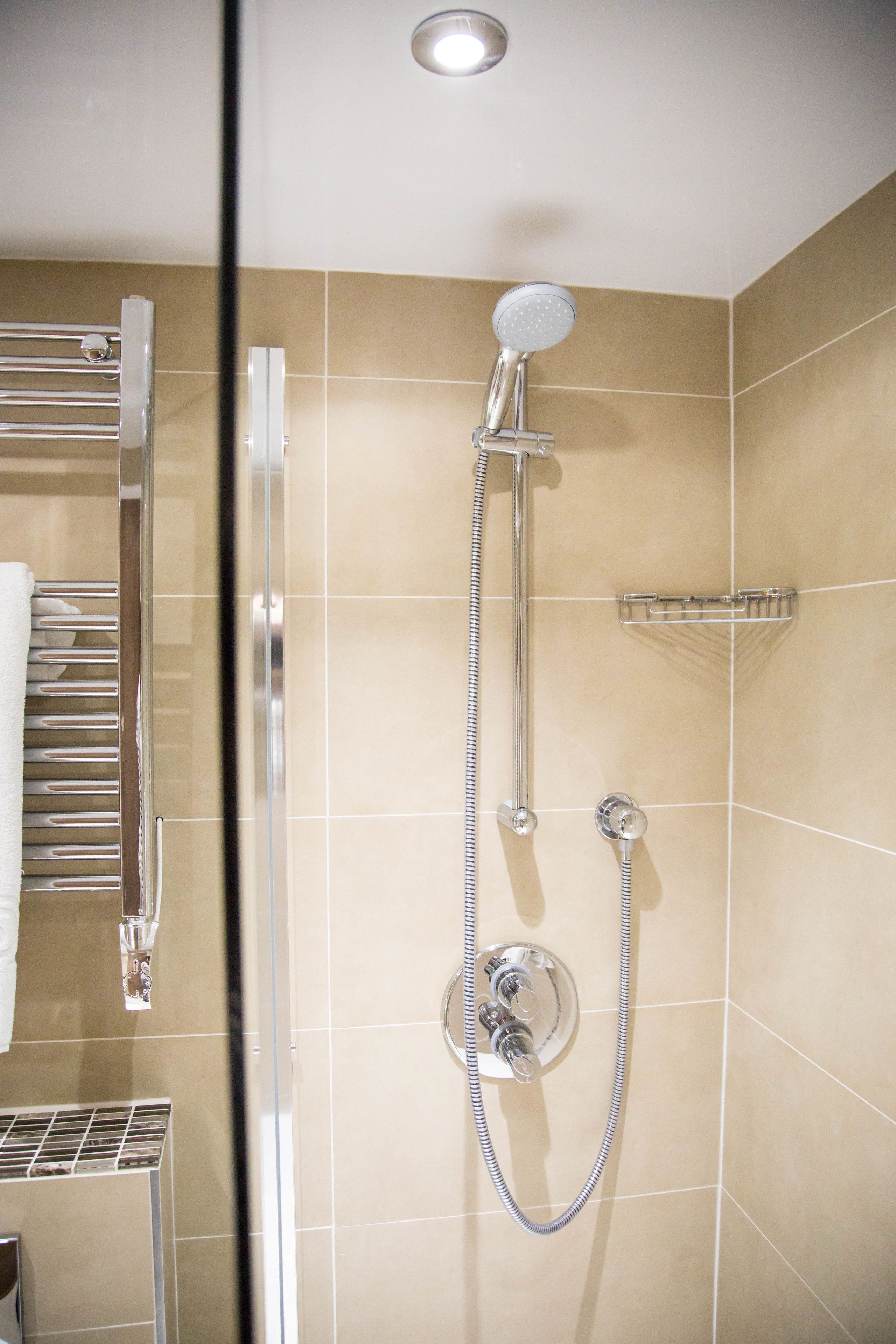 A shower with a handheld showerhead and a wall-mounted control.
