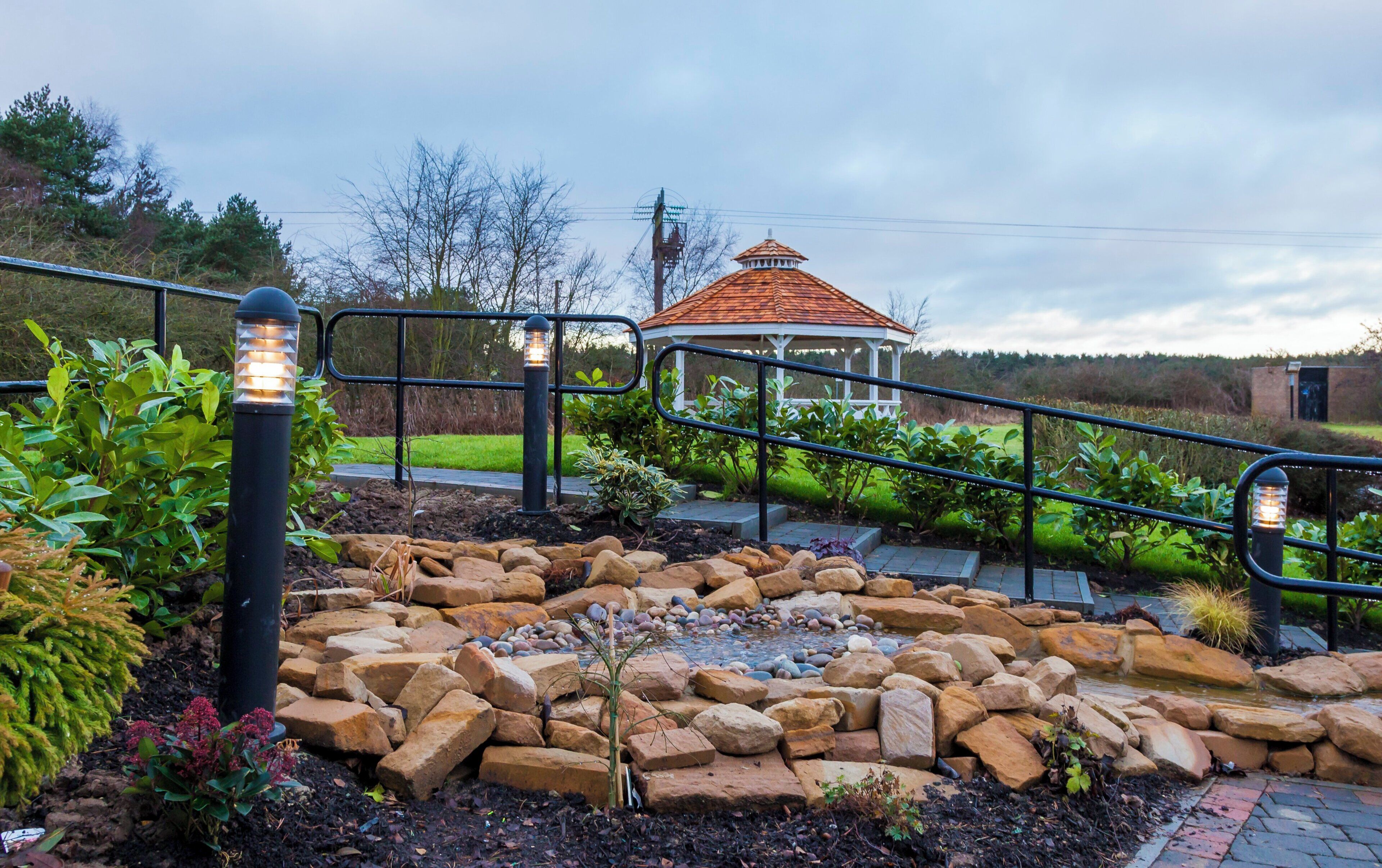 A garden with a gazebo, a stone pathway, and a metal railing.