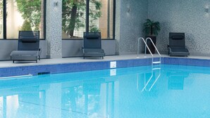 An indoor swimming pool with clear blue water, four lounge chairs, a potted plant, and a tiled wall with a tree reflection. - Holiday Inn Newcastle - Gosforth Park by IHG (Newcastle-upon-Tyne)