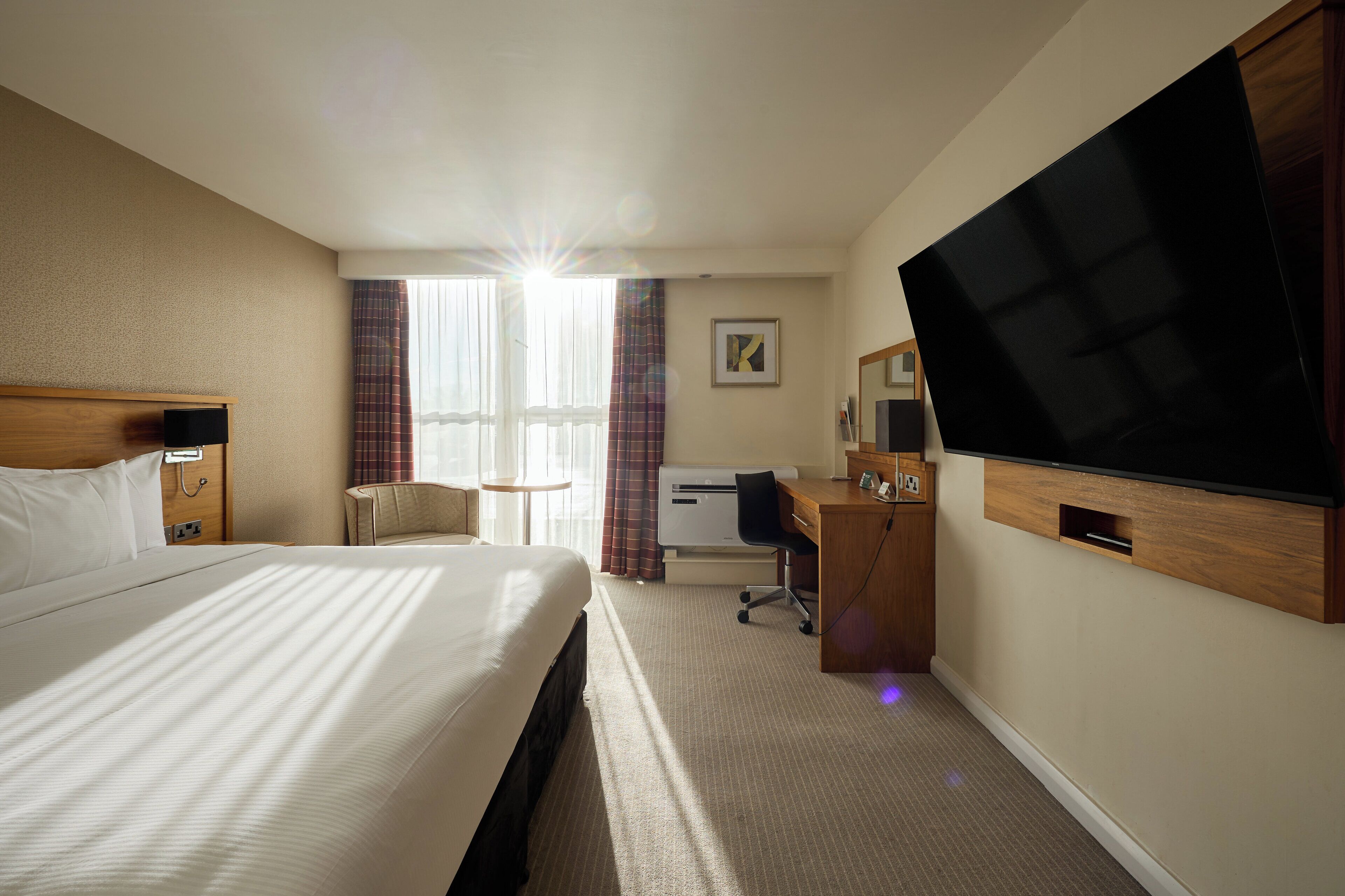 Habitación de hotel con una cama grande, un escritorio con computadora, televisión y ventana con cortinas.