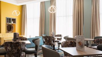 Un hall d’hôtel avec un mur jaune, une grande fenêtre avec des rideaux et différents types de sièges, notamment des canapés et des fauteuils.