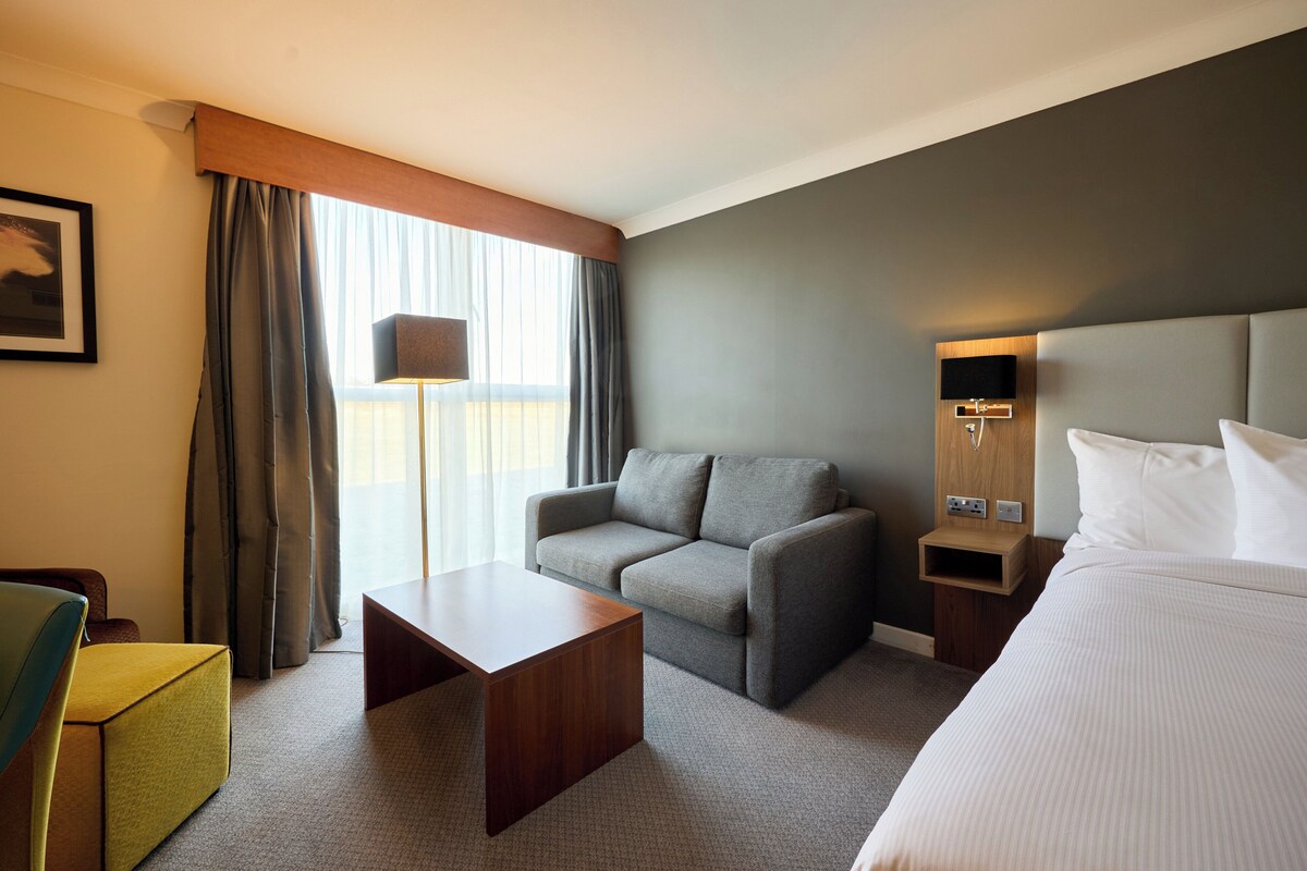 A hotel room with a bed, a sofa, a coffee table, a TV, and a lamp.