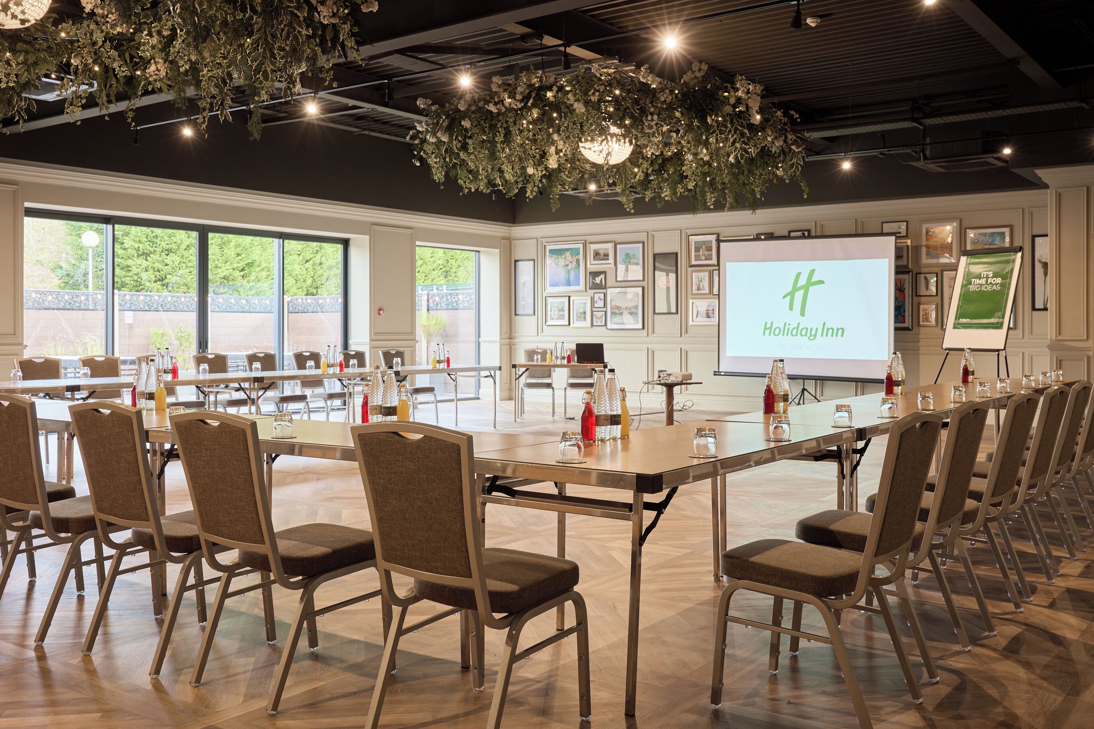 Ein Konferenzraum mit einem großen Tisch, Stühlen und einem Bildschirm, der 'Holiday Inn' anzeigt.