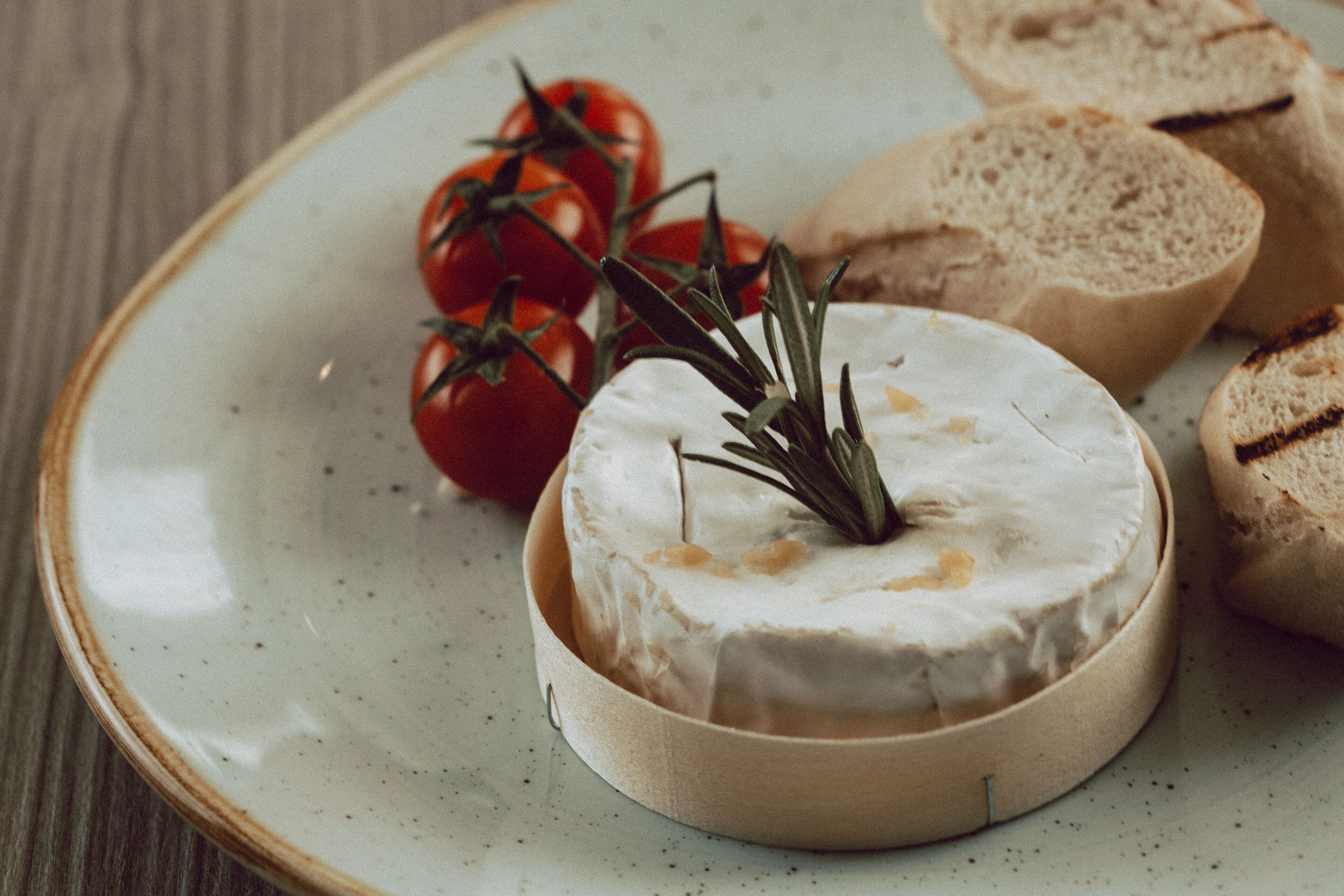 A round cheese wheel on a ceramic plate with grilled bread and cherry tomatoes.