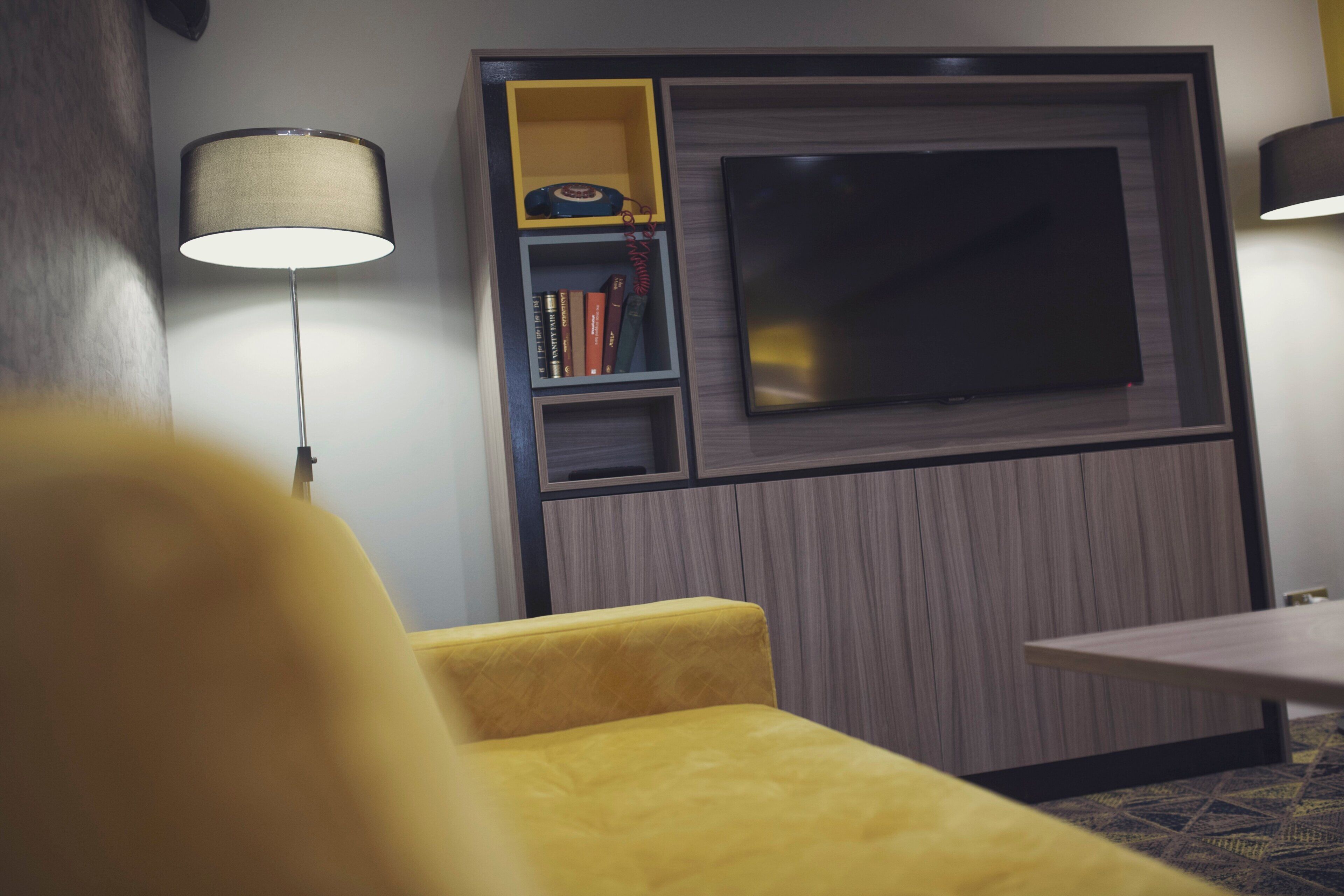 Una habitación moderna con televisor de pantalla plana, una estantería y un sillón amarillo.