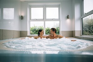 A couple in a hot tub with a view of greenery outside.