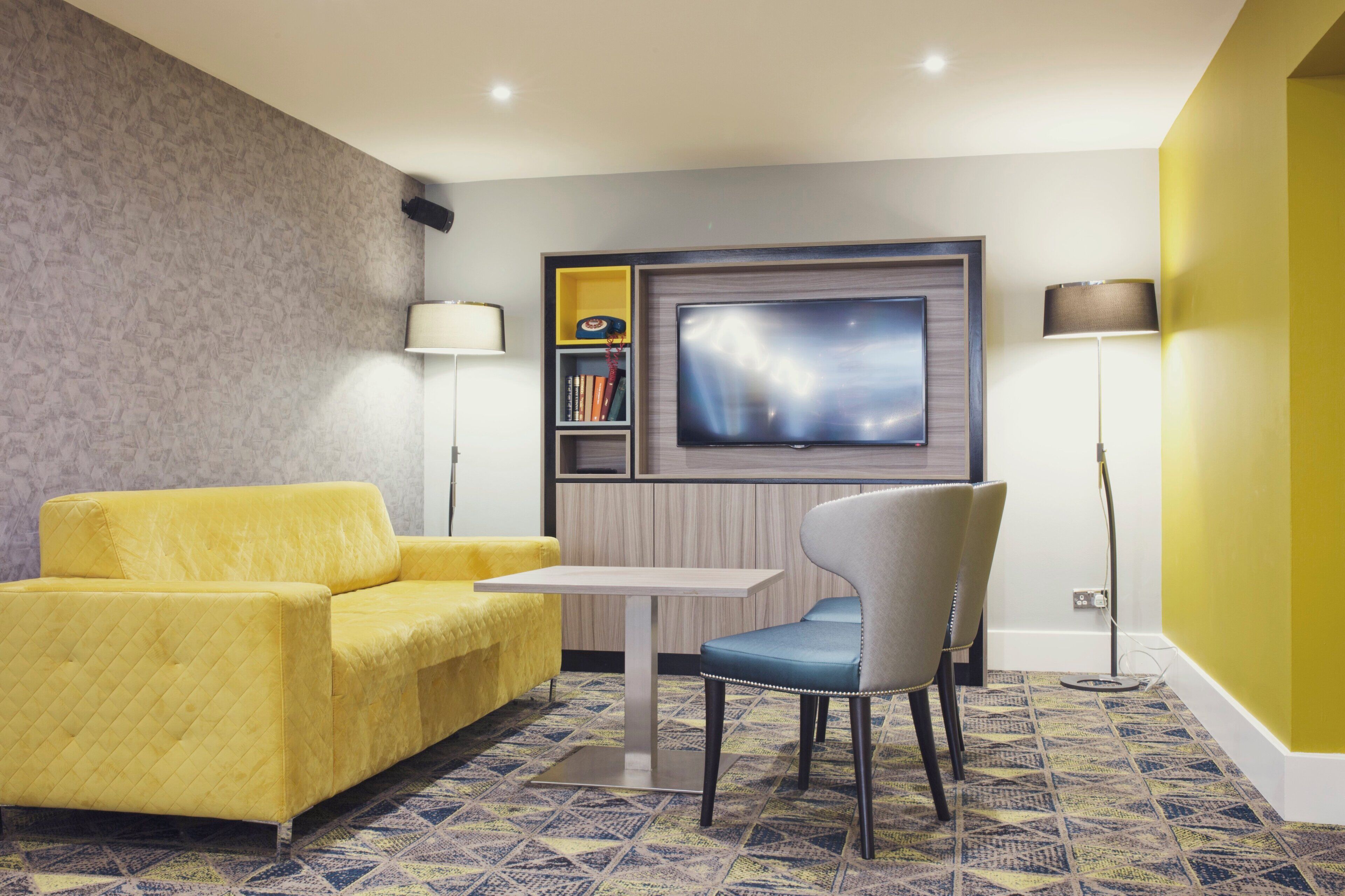 Una sala de estar moderna con un sofá amarillo, un sillón azul, un televisor de pantalla plana y una estantería.