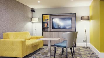 Una sala de estar moderna con un sofá amarillo, un sillón azul, un televisor de pantalla plana y una estantería.