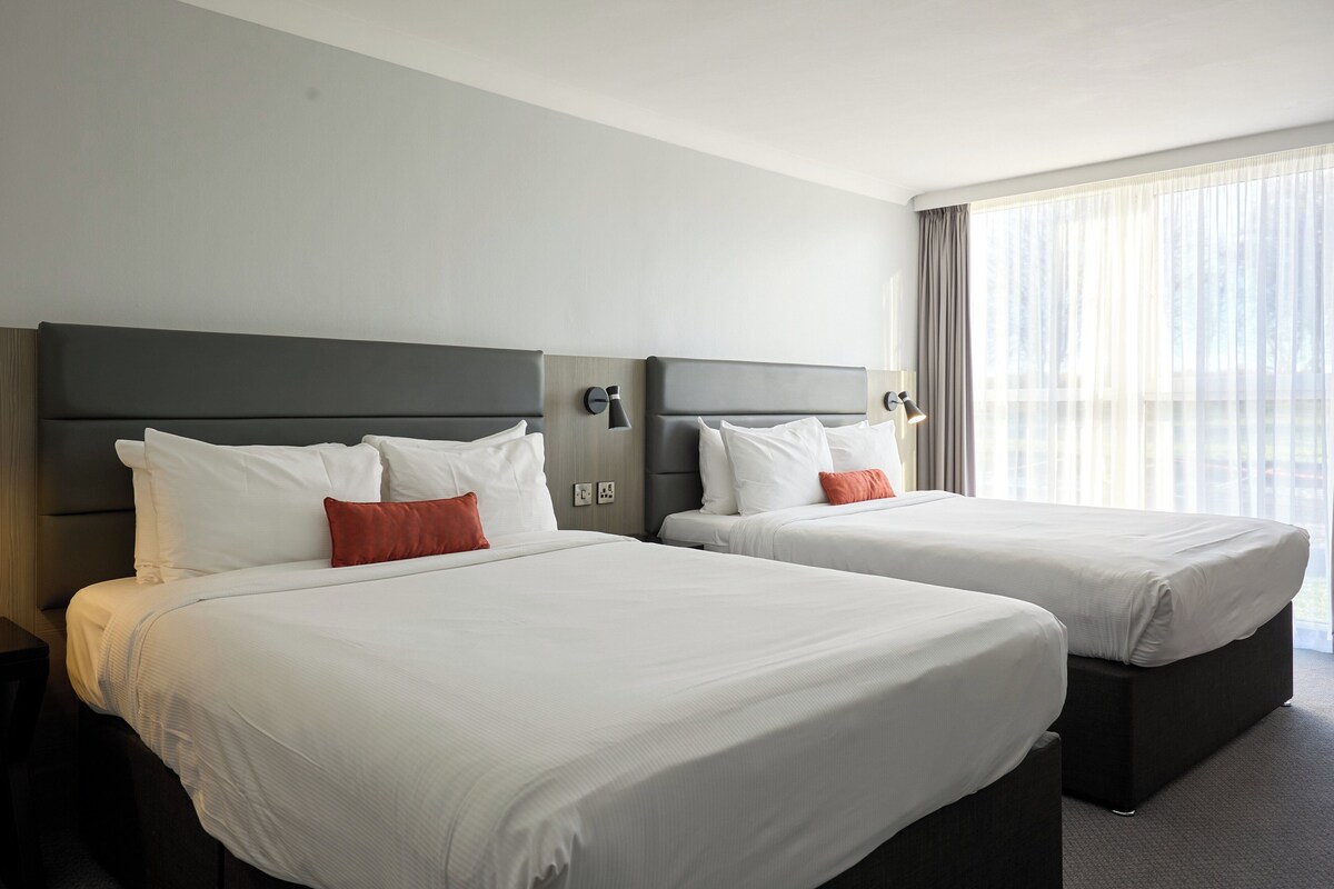Two single beds with grey headboards, white bedding, and a red pillow.