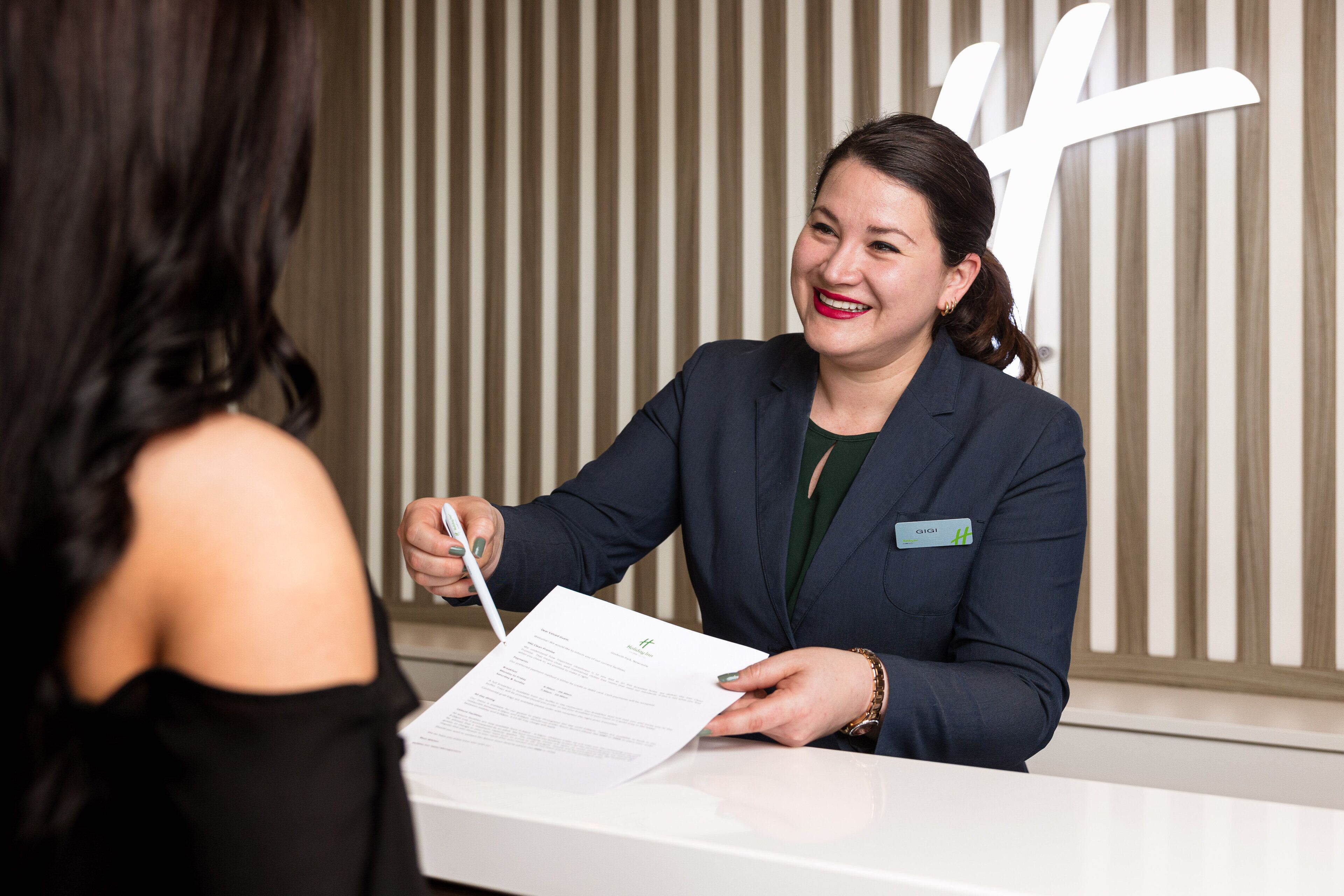 A reception desk with a person holding a document, likely a guest check-in form, in a hotel lobby with vertical striped wallpaper.
