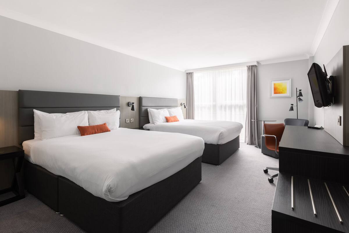A hotel room with two beds, a desk, a chair, a TV, and a window with curtains.