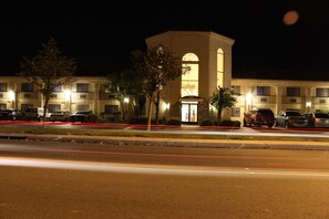 A hotel with a central tower, multiple balconies, and a parking lot at night.