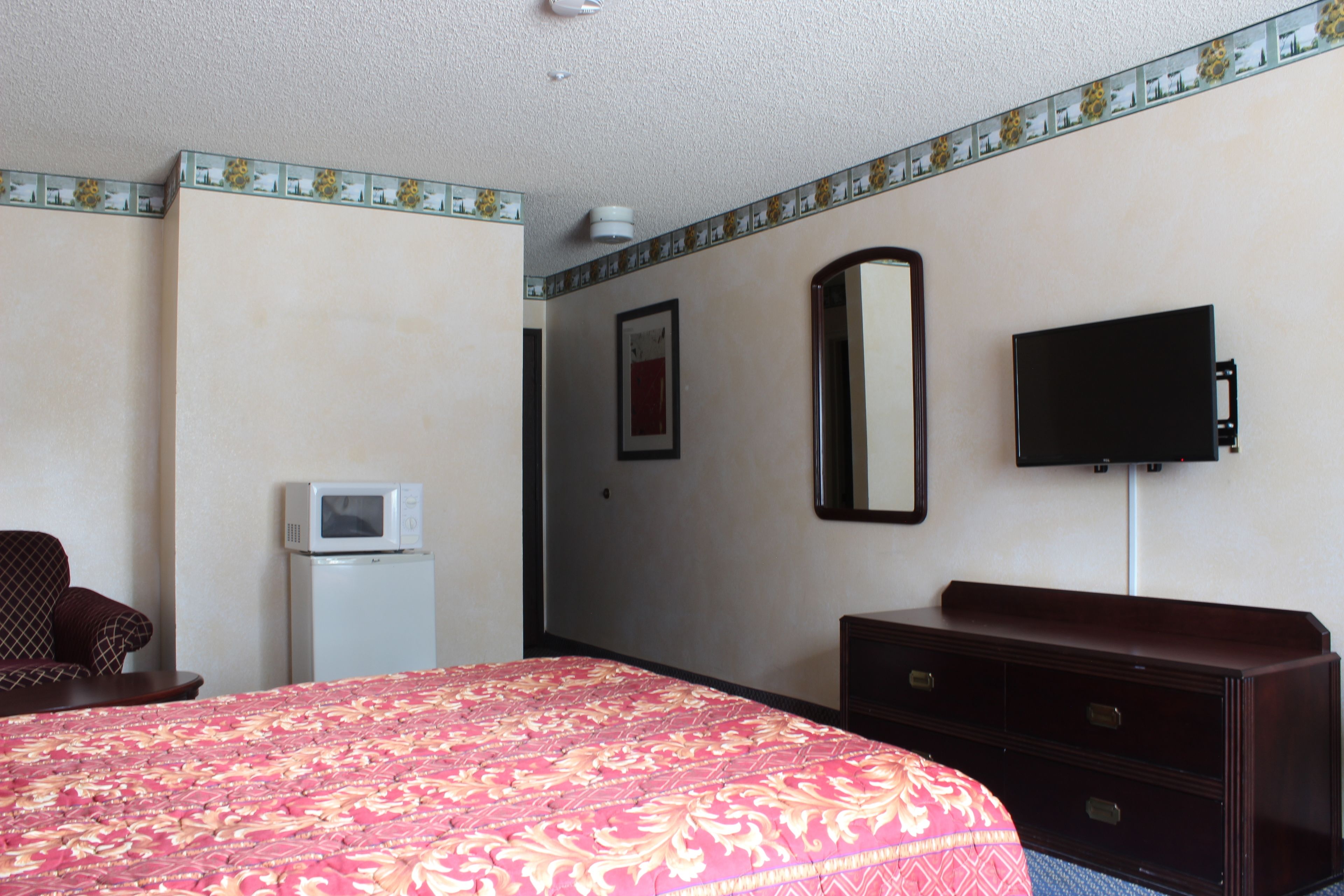 A hotel room with a bed, a dresser, a television mounted on the wall, and a small refrigerator.