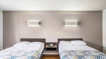 A hotel room with two single beds, a wooden nightstand with a phone, and two wall-mounted lights.