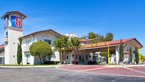 A motel with a prominent '6' sign, a covered parking area, and a well-maintained lawn. - Motel 6 Dallas, TX - Market Center (Dallas)