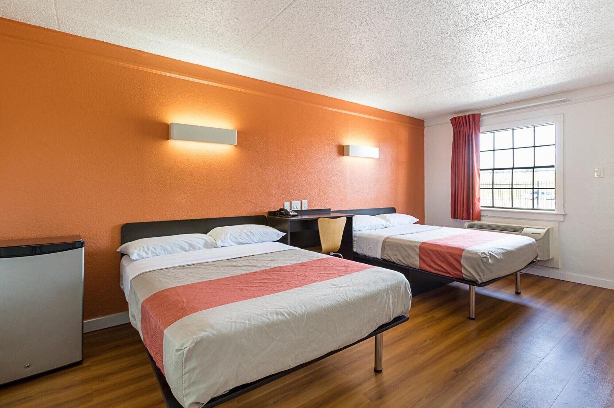 A hotel room with two beds, a desk, a chair, a window with a view, and a ceiling light.