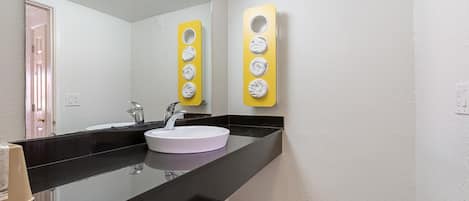 Un bagno moderno con un lavandino bianco, un piano di lavoro nero e uno specchio. Due erogatori di asciugamani gialli sono montati sulla parete.
