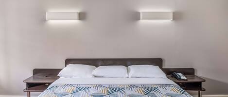 Una habitación de hotel con una cama, dos mesitas de noche y dos lámparas de pared.
