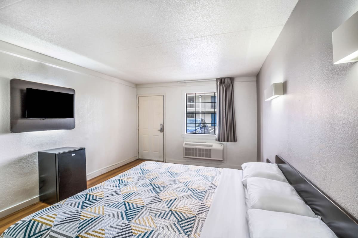 Hotelkamer met een bed, een flatscreen televisie aan de muur, een raam met gordijnen en een kleine verwarming bij het raam.