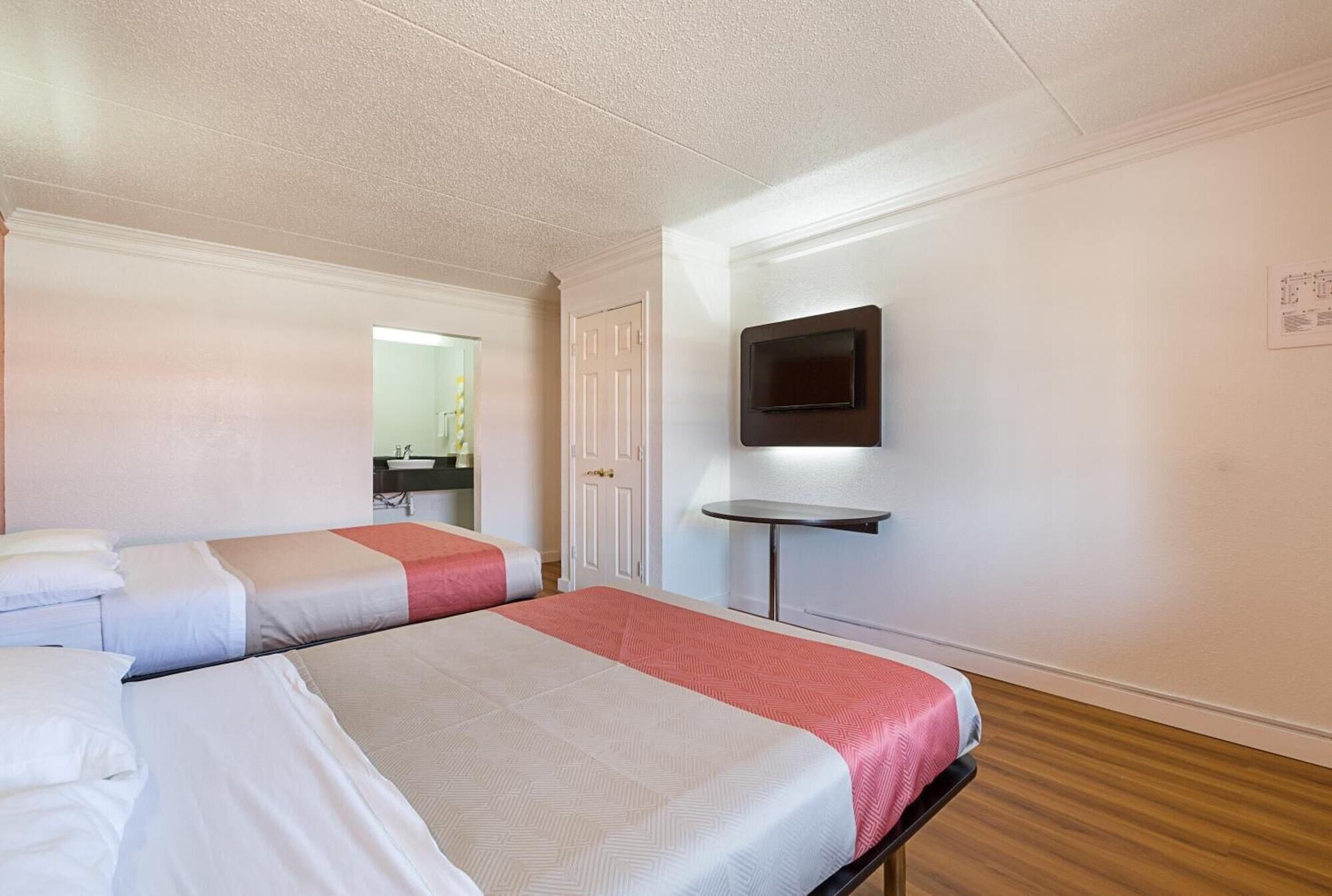 Una camera d'albergo con due letti, una TV a muro e un tavolino.