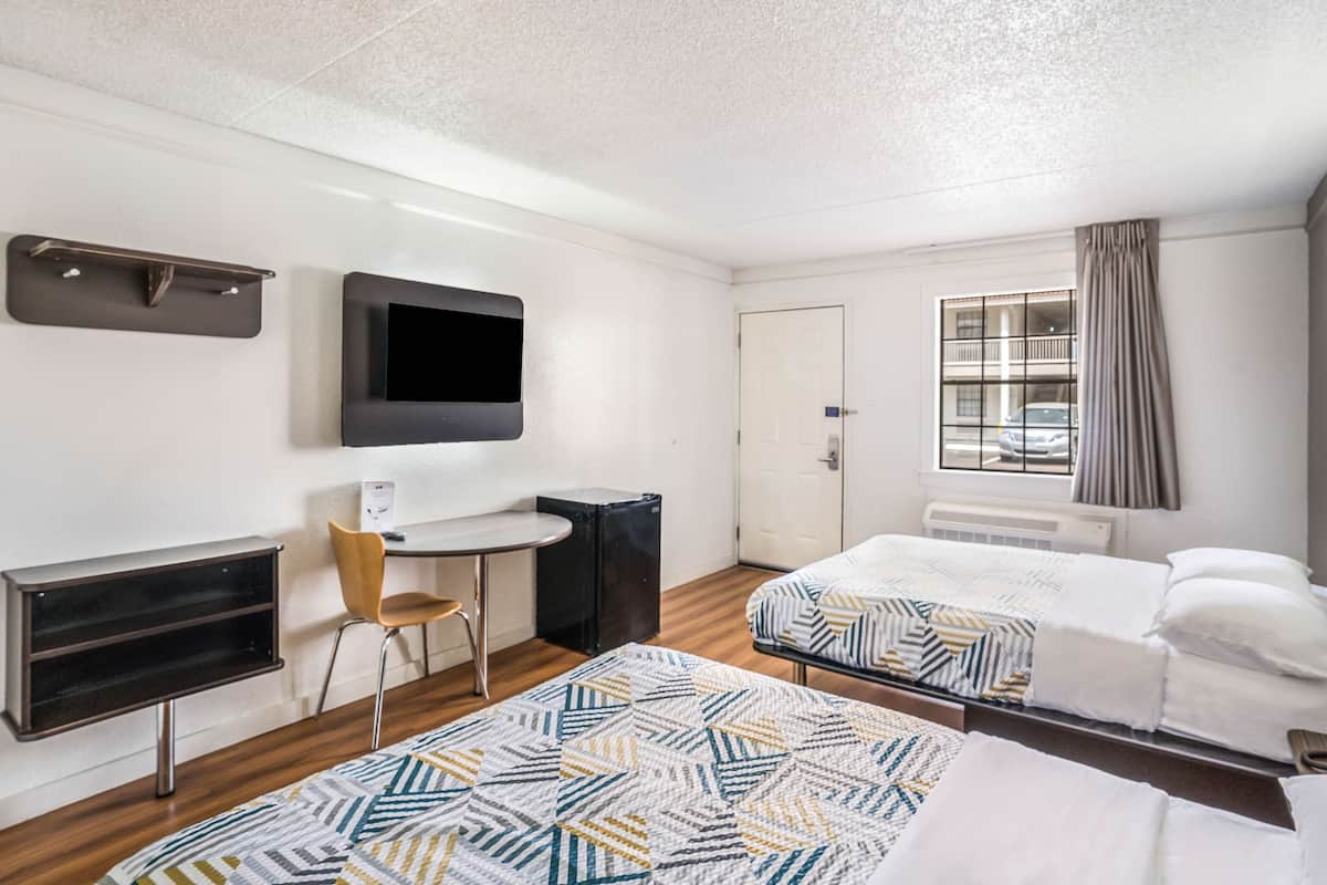 Een hotelkamer met twee bedden, een bureau, een stoel, een televisie en een raam met gordijnen.