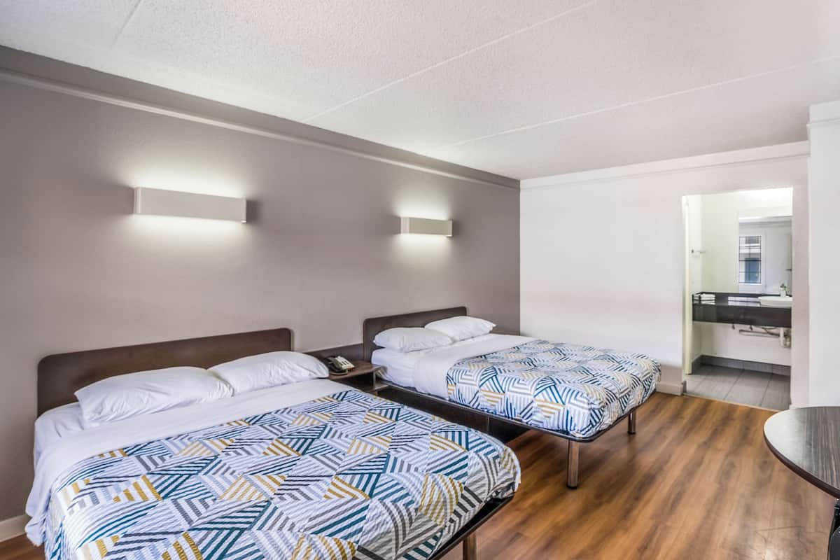 Een hotelkamer met twee bedden, een houten vloer, een badkamer met een wastafel en spiegel, en wandlampen.
