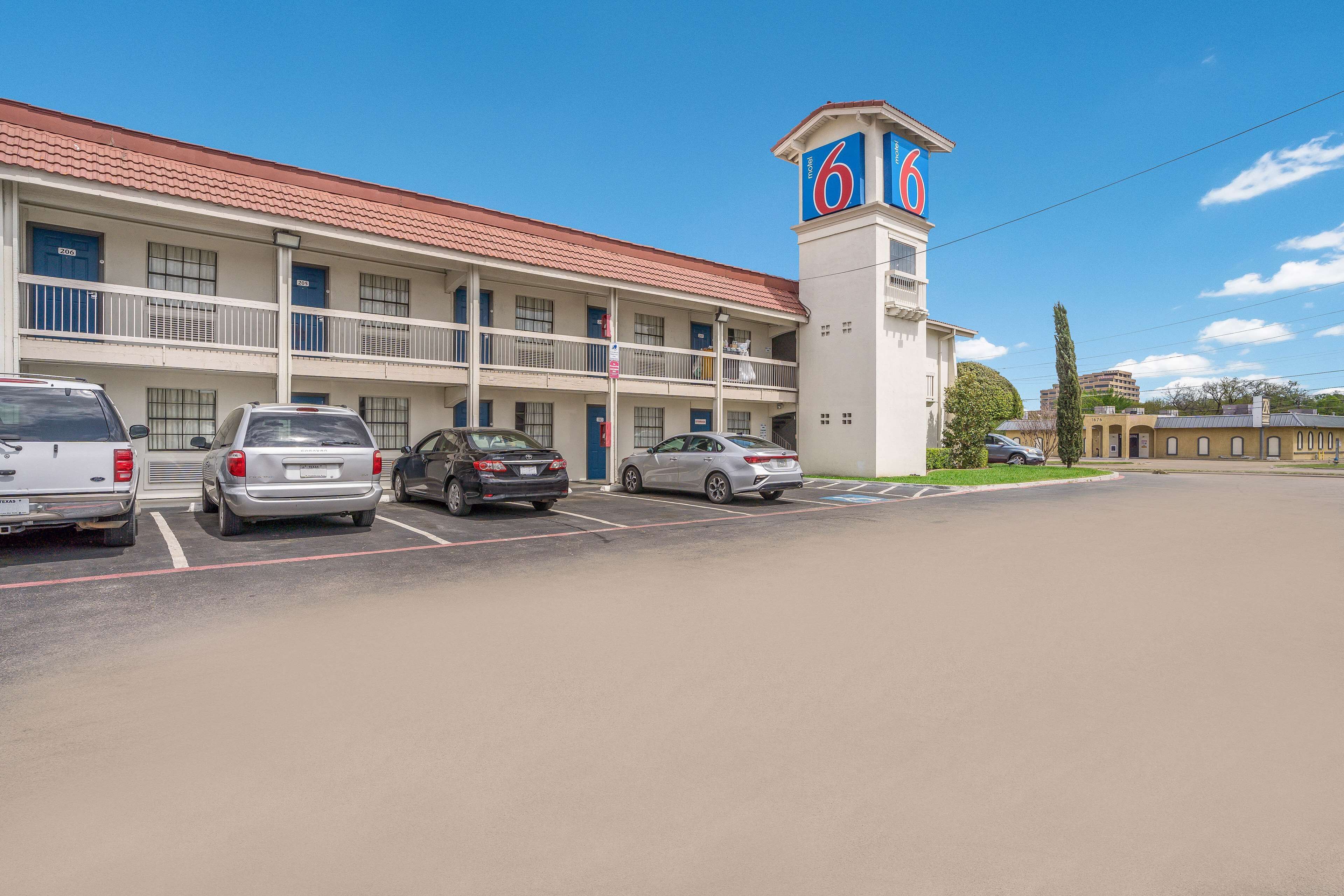 A motel with a red-tiled roof, a prominent '6' sign, and a parking lot with several cars.