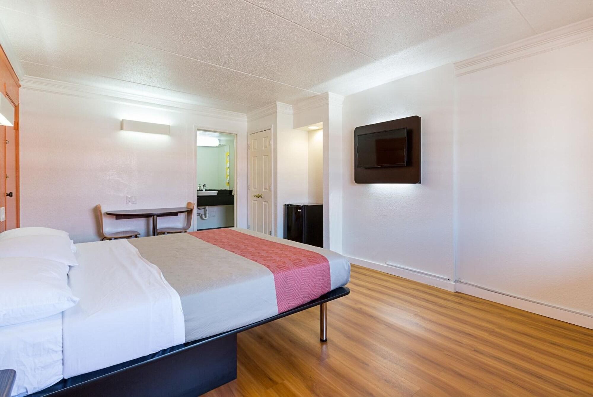 A hotel room with a bed, a desk, a TV, and a small kitchenette.