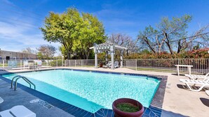 A rectangular swimming pool with a tiled edge, surrounded by a metal fence. There are lounge chairs and a gazebo in the background. - Motel 6 Dallas, TX - Market Center (Dallas)