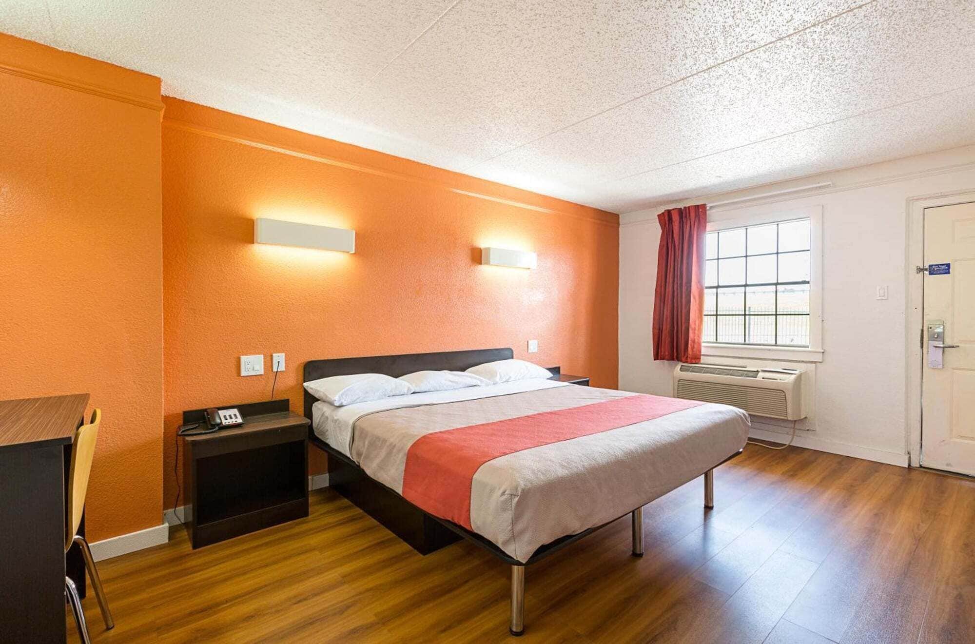 A hotel room with a bed, bedside table, lamp, and a window with curtains.