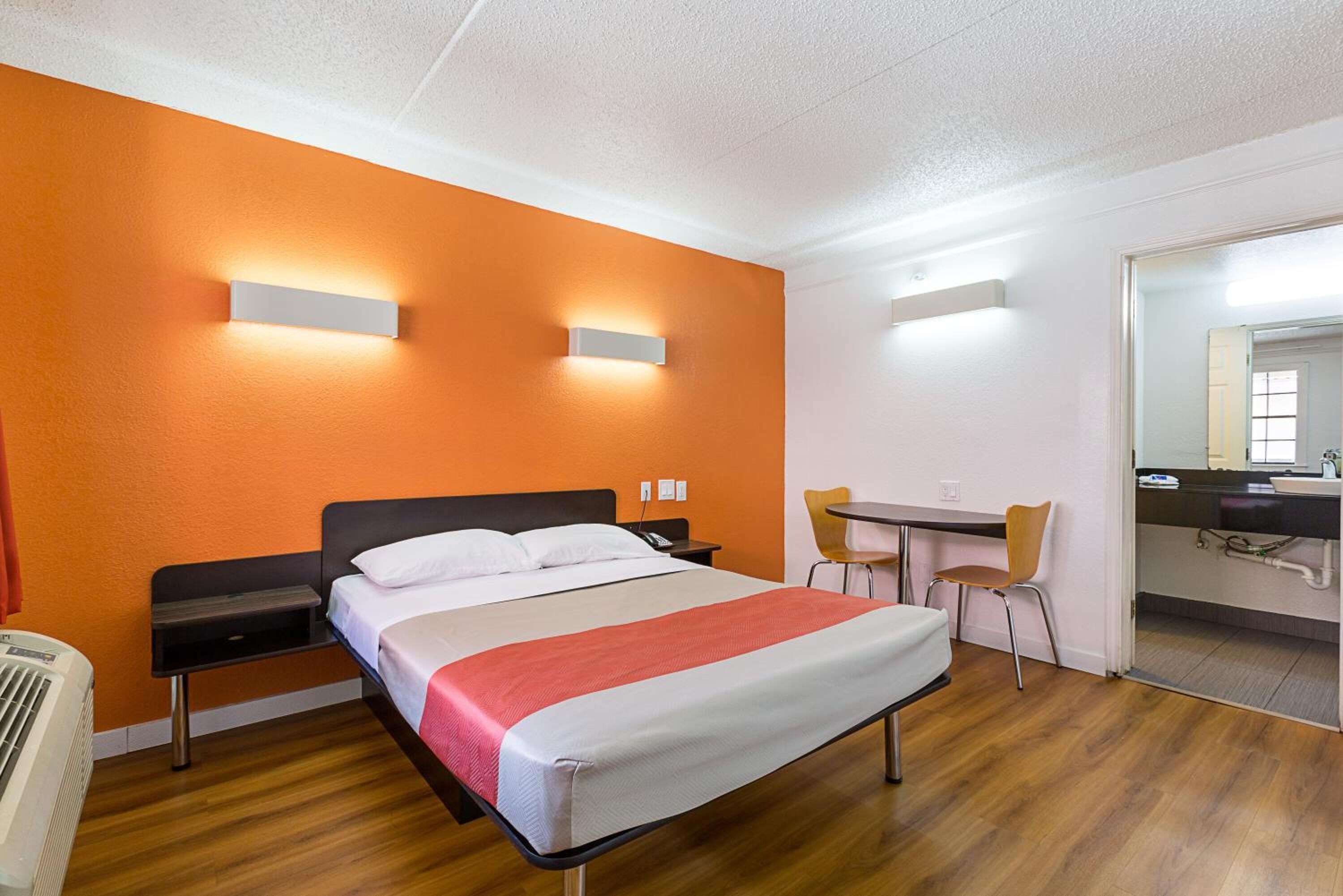 Une chambre d’hôtel avec un lit, des tables de chevet, un bureau, une chaise et une salle de bain visible à travers une porte ouverte.