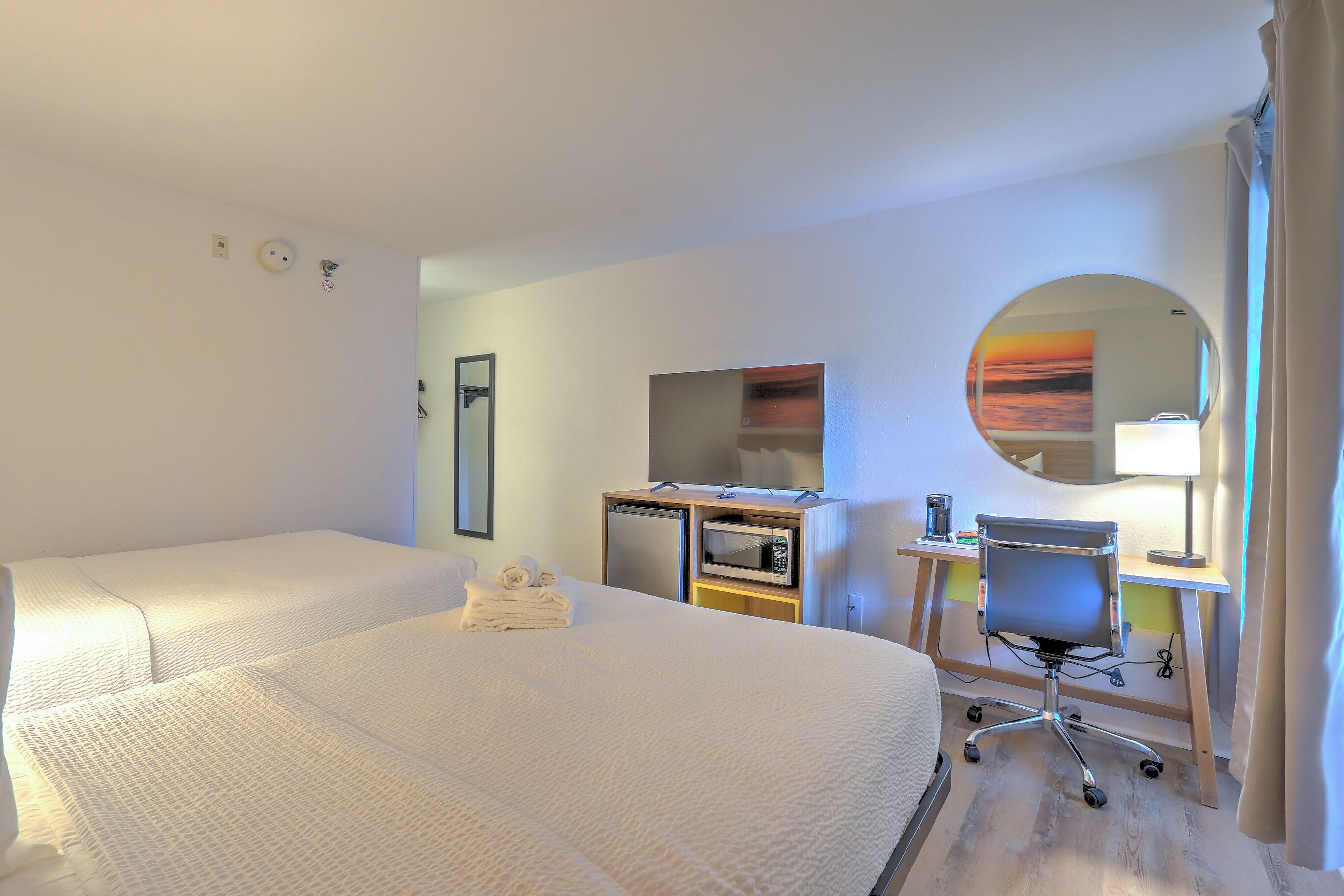 Quarto de hotel com duas camas, uma escrivaninha com computador, micro-ondas e um pequeno frigorífico.