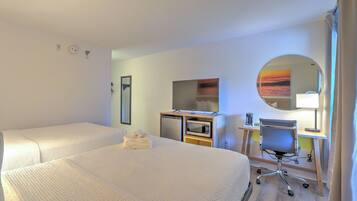 Quarto de hotel com duas camas, uma escrivaninha com computador, micro-ondas e um pequeno frigorífico.