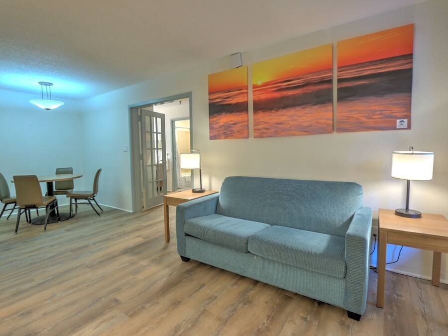 A living room with a sofa, two side tables, a coffee table, and chairs. There are two wall-mounted lamps and a ceiling light.