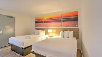 Et hotelværelse med to senge, et træhovedgærde, et maleri af en solnedgang og et natbord med en lampe.