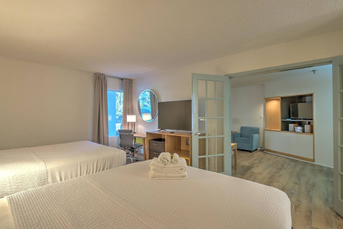 A hotel room with two beds, a desk with a computer, a chair, and a TV.