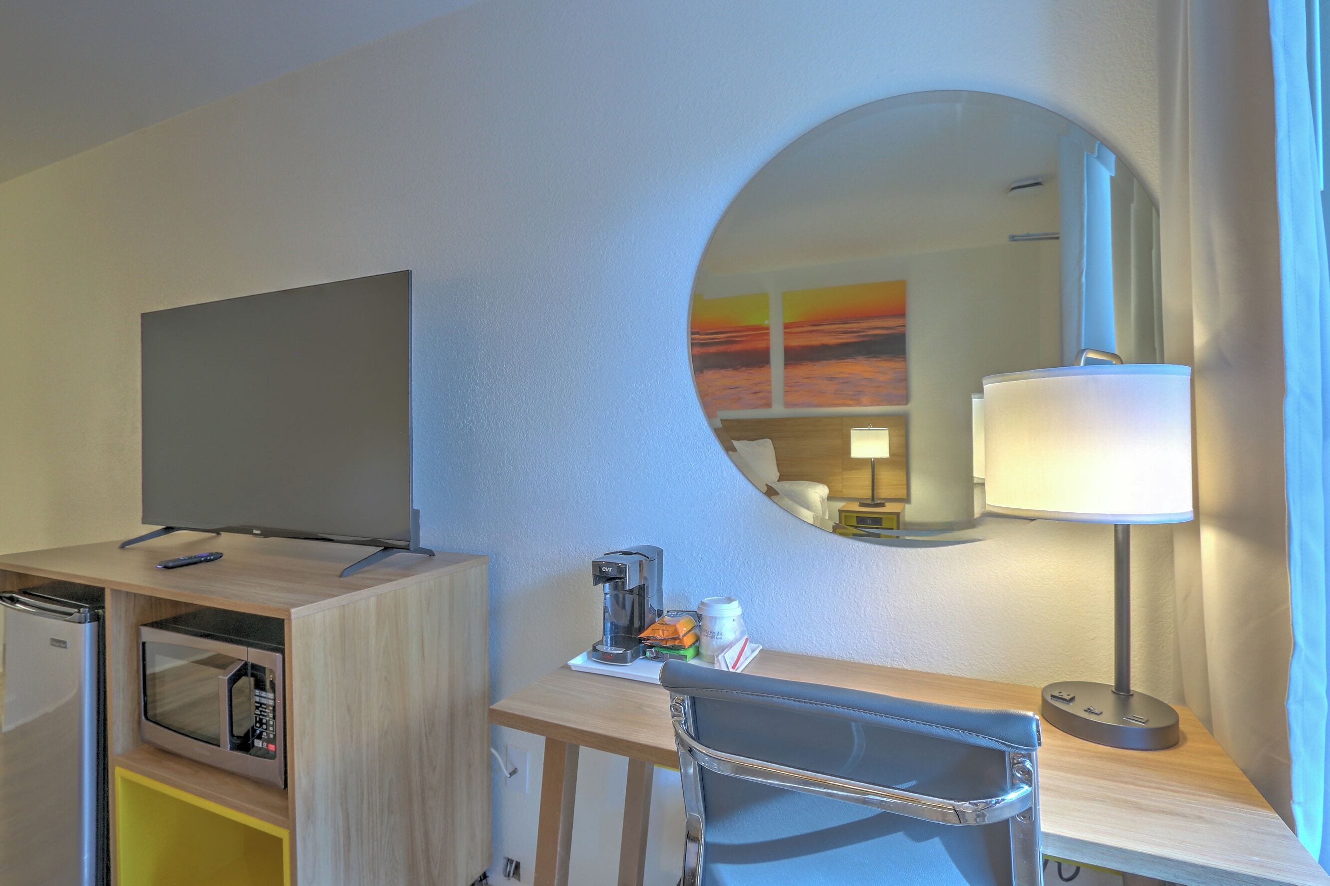 A hotel room with a flat-screen TV, a microwave, a coffee maker, a lamp, and a chair.