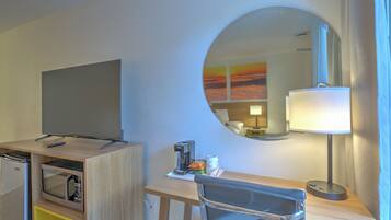 A hotel room with a flat-screen TV, a microwave, a coffee maker, a lamp, and a chair.
