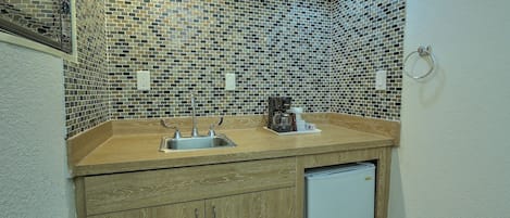 A kitchen with a wooden countertop, two sinks, a coffee maker, and a small refrigerator.